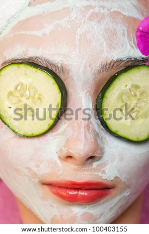 Cute young girl getting pampered with a deluxe spa treatment including facial mask and sliced cucumber over her eyes.