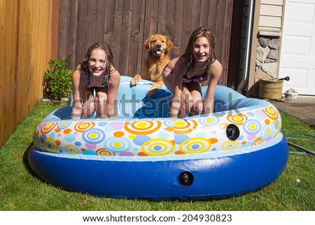 Two young girls and their pet Golden retriever playing in an inflatable swimming pool during the summer