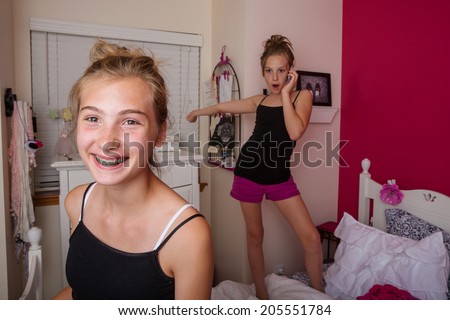 Two young girls playing and talking on the phone in their pink bedroom.