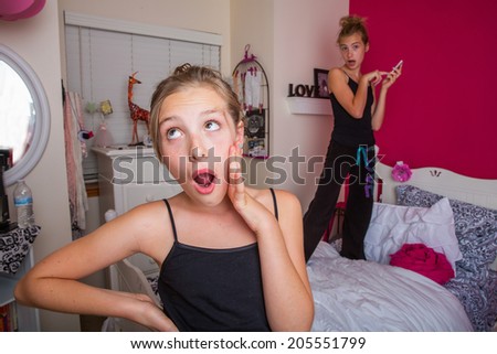 Two young girls playing and talking on the phone in their pink bedroom.