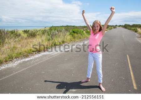 A pretty teenage girl raising her arms in victory on an empty country road