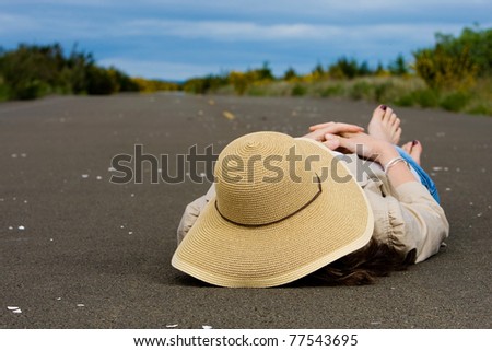a woman laying down asleep in the middle of a long empty road