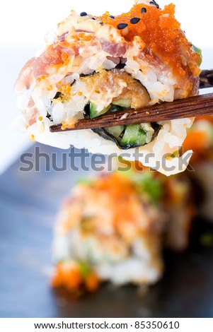 A colorful Japanese sushi roll being held in the air chopsticks over a plate.  Asian food is delicious!