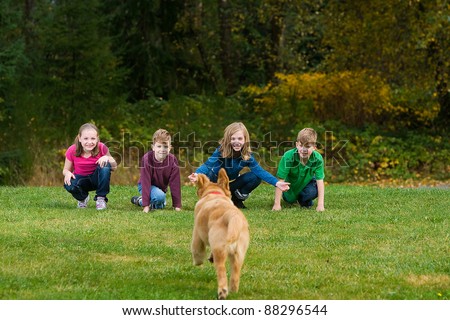 A group of children call a Golden Retriever puppy dog.  The dog is running towards them in a field of green grass.