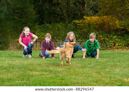 A group of children call a Golden Retriever puppy dog.  The dog is running towards them in a field of green grass.