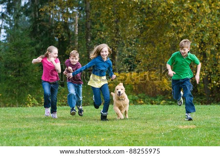 A group of 4 kids racing in a park with a dog.