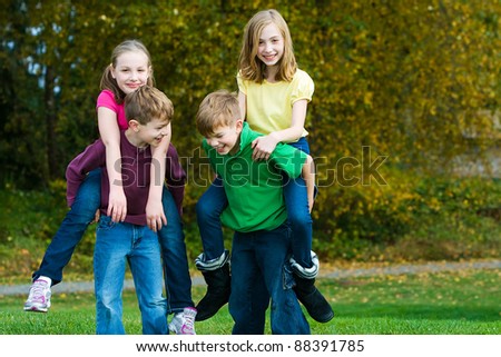 A group of active, healthy children giving each other piggy back rides outside.