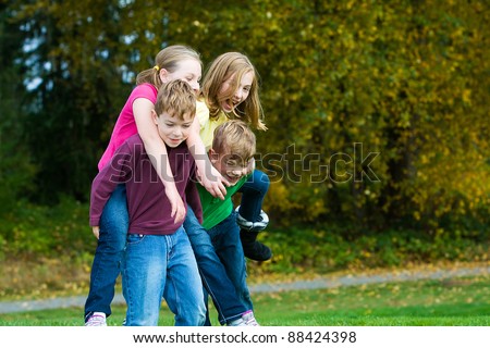 Happy young kids giving each other piggy back rides.  Playing and having fun actively outside.
