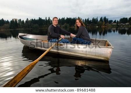 A happy couple rowing a small aluminum boat on a lake. A fun date