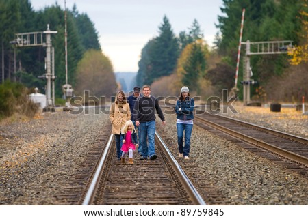 Group of people walking down train tracks outside on an Autumn day.