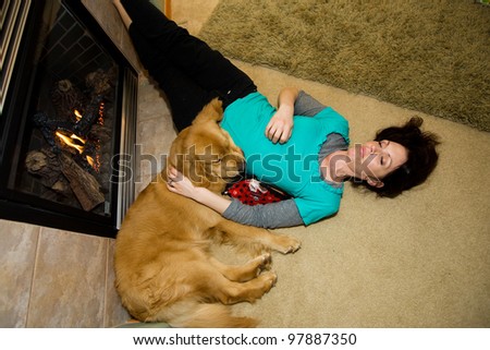 An exhausted woman sleeping comfortably next to a fire with her Golden Retriever dog.