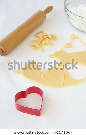 Cookie dough with heart shapes cut out of it with a red heart shaped cookie cutter