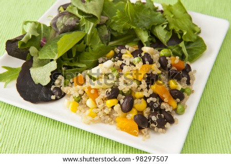 Plate of quinoa vegetable salad and field greens on a green tablecloth