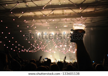 Shot of some fans during a life concert of a famous british band. Focus on a happy man with a beer on his hand.