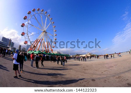 People and a ferris wheel at a Festival. People come up to the ferris wheel and watch the concerts from the heights.