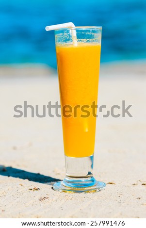 Glass of mango juice at the beach on the sand