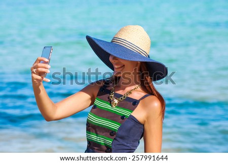 summer vacation, holidays, travel, technology and people concept - young woman on beach making selfie with smartphone over blue sky background