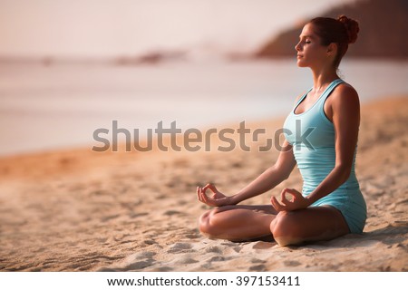 Young beautiful healthy woman making meditation on the beach, sunset on the sea.