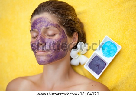 Beautiful happy woman in a tropical spa making face mask treatment