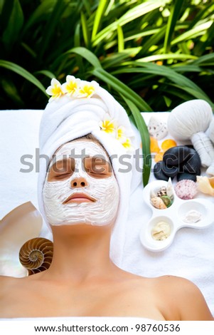 Young beautiful woman in tropical spa making face mask treatment