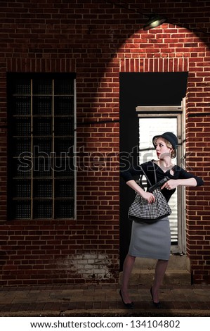 Beautiful scared woman pulling out a gun in a dark alley