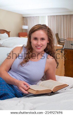 Beautiful young woman reading a book in bed