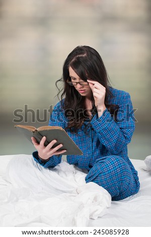 Beautiful young woman reading a book in bed