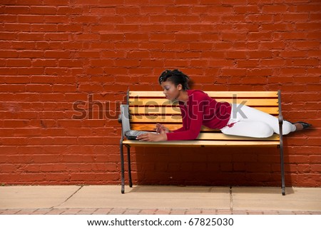 A beautiful black woman college student on a downtown park bench working on a computer