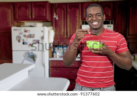 Young black African American man eating food from a bowl in a home kitchen