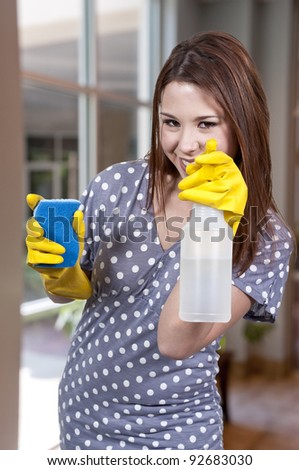 A glove wearing beautiful woman or maid cleaning house with a sponge and spray bottle with cleaner