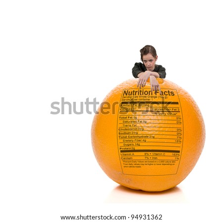 A beautiful young teenage woman standing behind an orange with a nutrition label
