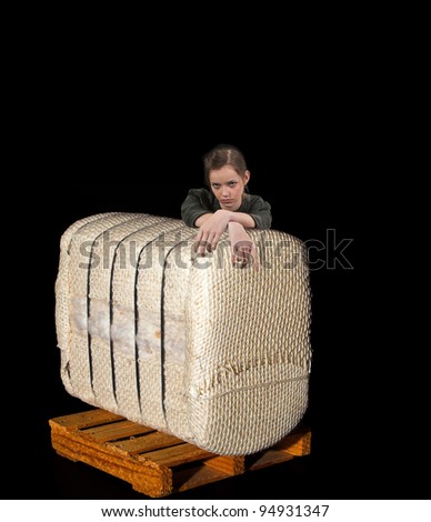 A beautiful young teenage woman leaning on a bale of raw cotton on a pallet