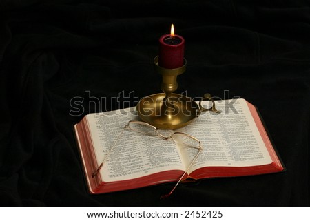 Candle in candleholder on an open Bible surrounded by darkness showing whole Bible