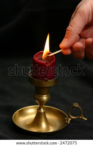 Man\'s hand lighting candle with match on the wick