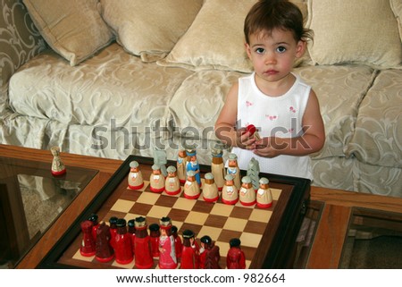 Close-up of a beautiful one-year-old baby girl playing with chess pieces.