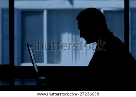 A man sitting in front of his laptop against the evening window.