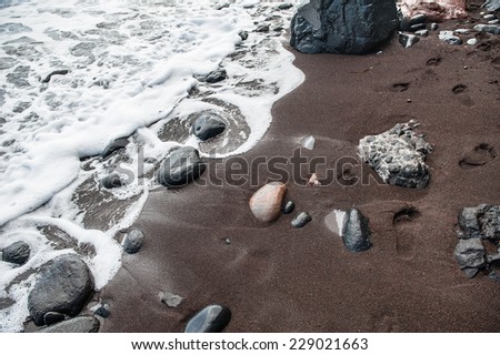 Footprints in the sand. Black sand on the Red Beach. Santorini island, Greece.