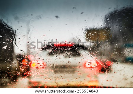 Car lights through the wet windshield. Street in the rush hour. Bokeh abstract lights background. Small depth of sharpness.