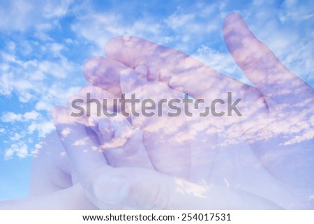 Sweet baby feet in his father hands in double exposure with cirrus clouds against the blue sky background
