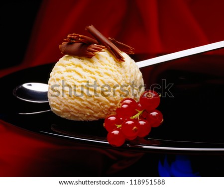 Ball of vanilla ice cream with chocolate curls and currants on a plate
