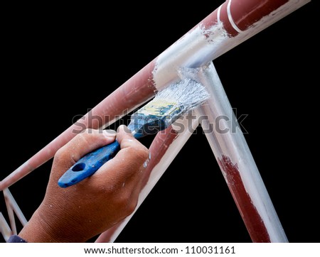 young man hand with flat tip paintbrush is  painting silver color to the metal structure tube frame isolated on black with working path
