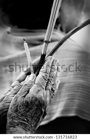 Faithful hands of old Buddhism holding candle lotus blossom and incense, black and white processed image.