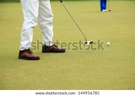 Golfer putting his putter club for a golf ball go straight to the hole