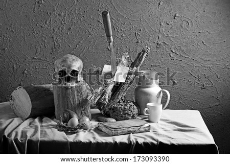 Still life art photography concept on voodoo straw doll stuck with knife on wood log and skull with black accessories black and white version