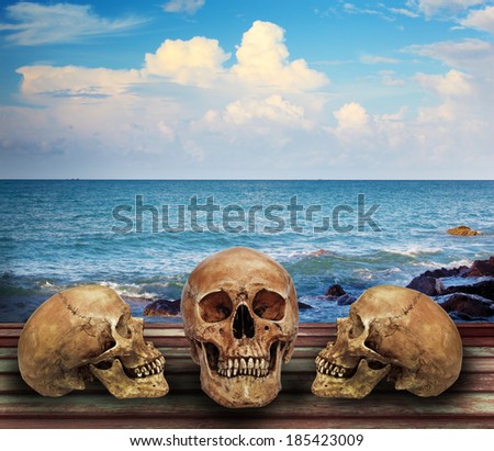 Three skulls on long bridge along blue sea cloudy sky