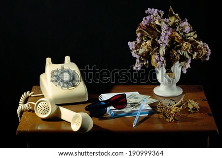 Still Life on wood table with vintage dial telephone dry flower bank note and note book