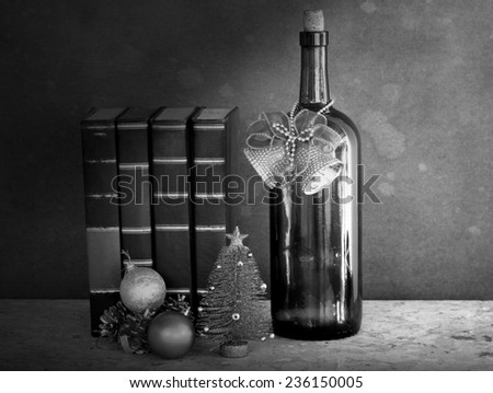 Old wine bottle wearing golden bells beside vintage books with mini Christmas tree a still life art style black and white version