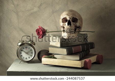Still life art photography love concept with human skull and books rose and alarm clock on wood toy cart over grunge background