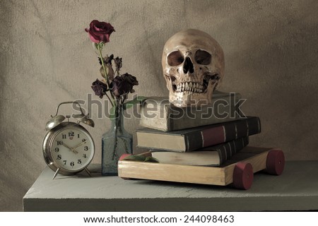 Still life art photography love concept with human skull and books rose and alarm clock on wood toy cart over grunge background