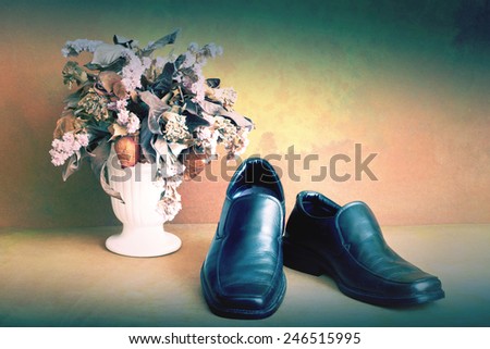 Black genuine shoes on grunge with dry flowers in vase still life art photography